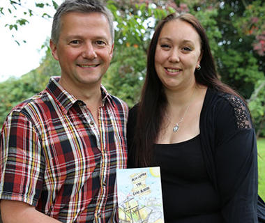 Man in checked shirt and woman in black top holding a book