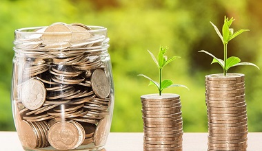 glass jar of coins and two piles of coins with sprouts of plants at the top