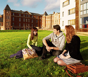 Three students sitting on the grass in front of city campus