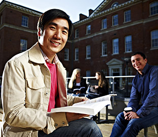 Two smiling students one of which is holding an opened book