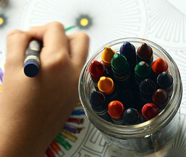 A close up shot of a child's hand colouring in a page next to a pot of colouring pencils.