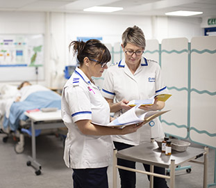 Two nurses in white uniforms discussing the contents of a folder
