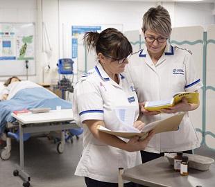 two women in nursing uniform reading from an open book