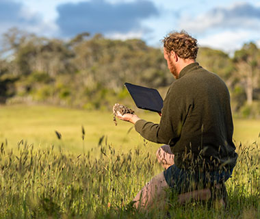 A farmer is kneeling down in a field in the sunshine