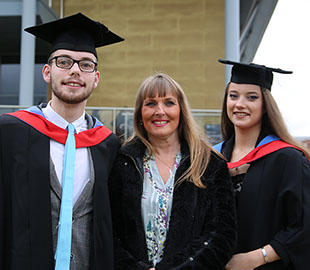 Two students in graduation robes aside a mature woman