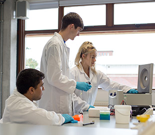 three students in white protective jackets and blue gloves